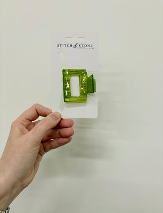 Hand holding a green plastic tool on a white background with 'Stitch & Stone' branding.