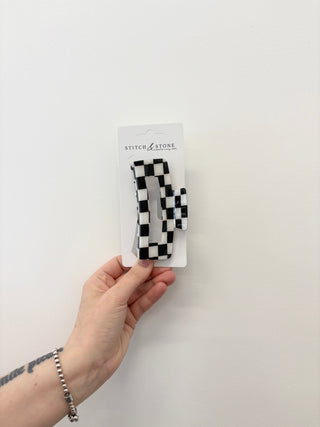 Hand holding a package of black and white checkered hair clips on a white background
