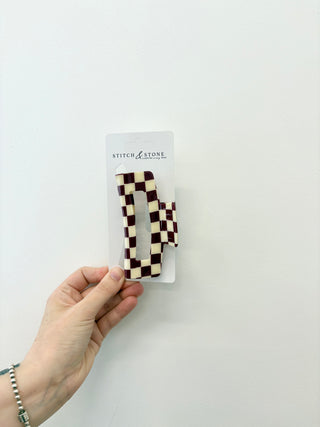 Checkered letter 'N' hair clip held by a hand on a white background