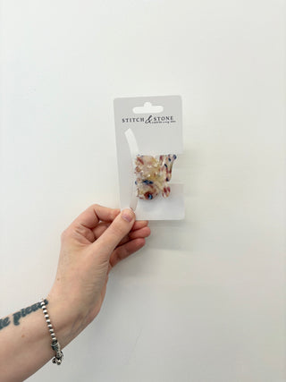 Hand holding a hair accessory package labeled 'Stitch & Stone' against a white background