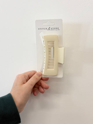 Hand holding a white hair clip in clear packaging with 'Stitch & Stone' branding on a white background.