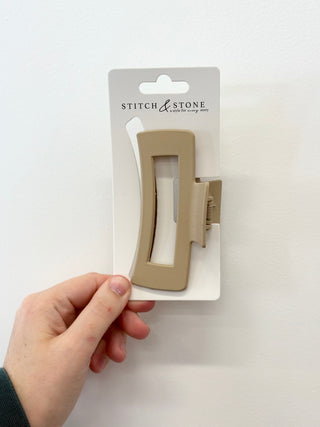 Hand holding a beige hair clip on a white background with 'Stitch & Stone' packaging.