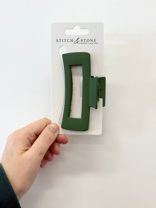 green  hair clip on a white card with 'Stitch & Stone' branding, held by a hand against a white background.