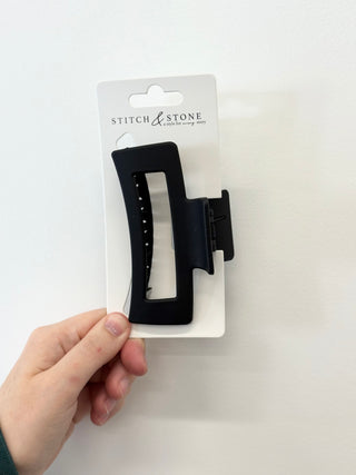 Black hair clip on a 'Stitch & Stone' branded card held by a hand against a white background