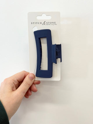 Blue hair clip on a white card with 'Stitch & Stone' branding, held by a hand against a white background.