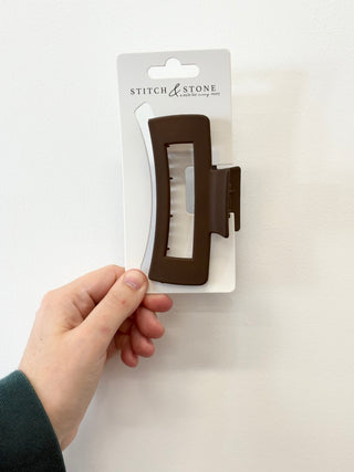 brown hair clip on a white card with 'Stitch & Stone' branding, held by a hand against a white background.