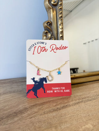 Jewelry card with gold necklace featuring horse, star, and pink boot charms on a wooden surface.
