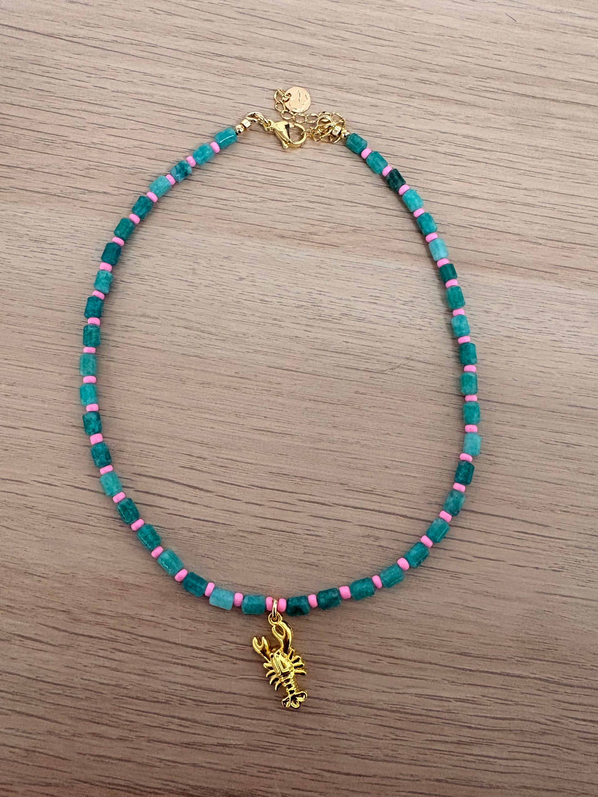 Necklace with green, pink, and gold beads on a wooden surface