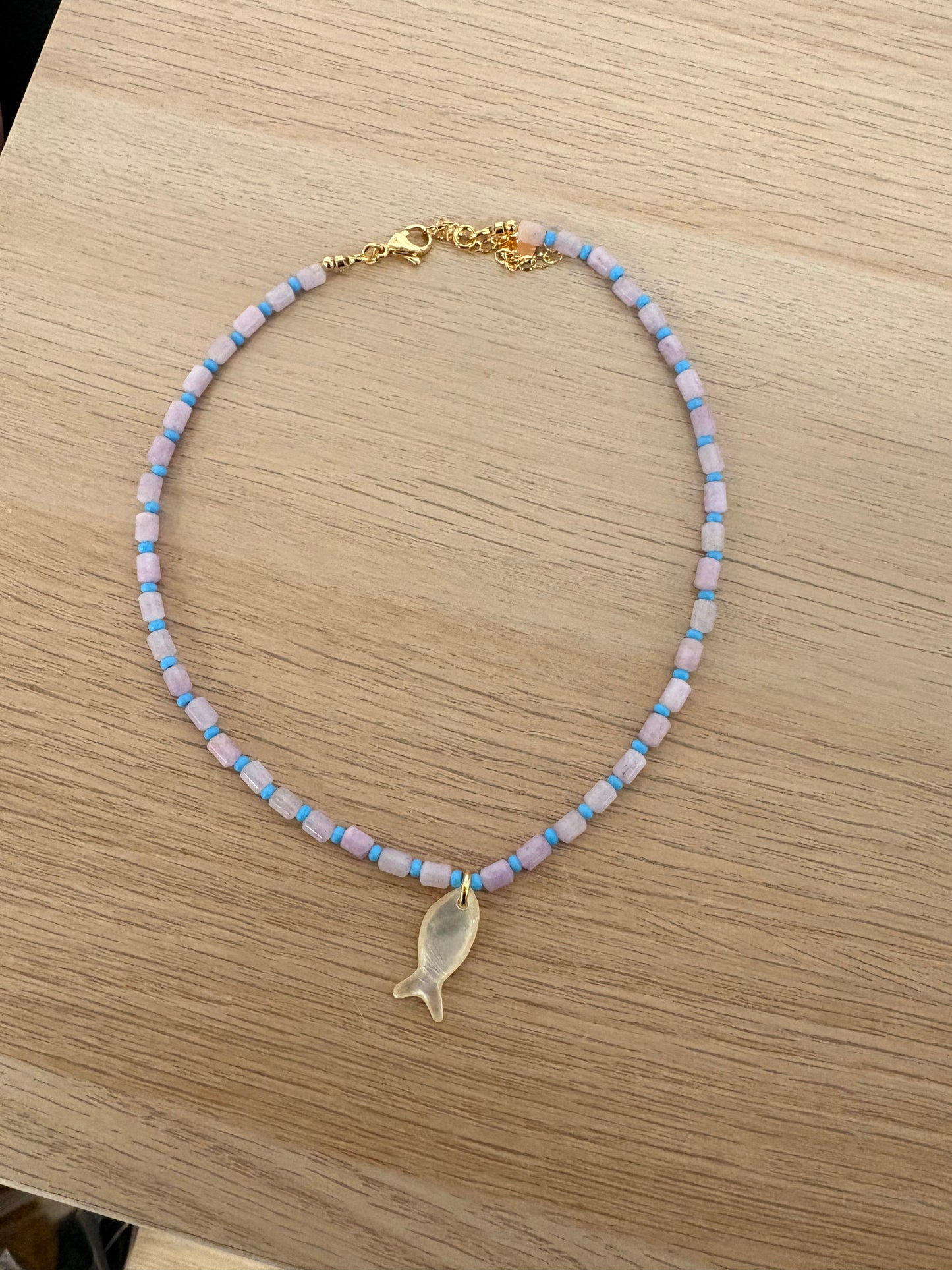 Necklace with beaded chain and gold fish pendant on a wooden surface