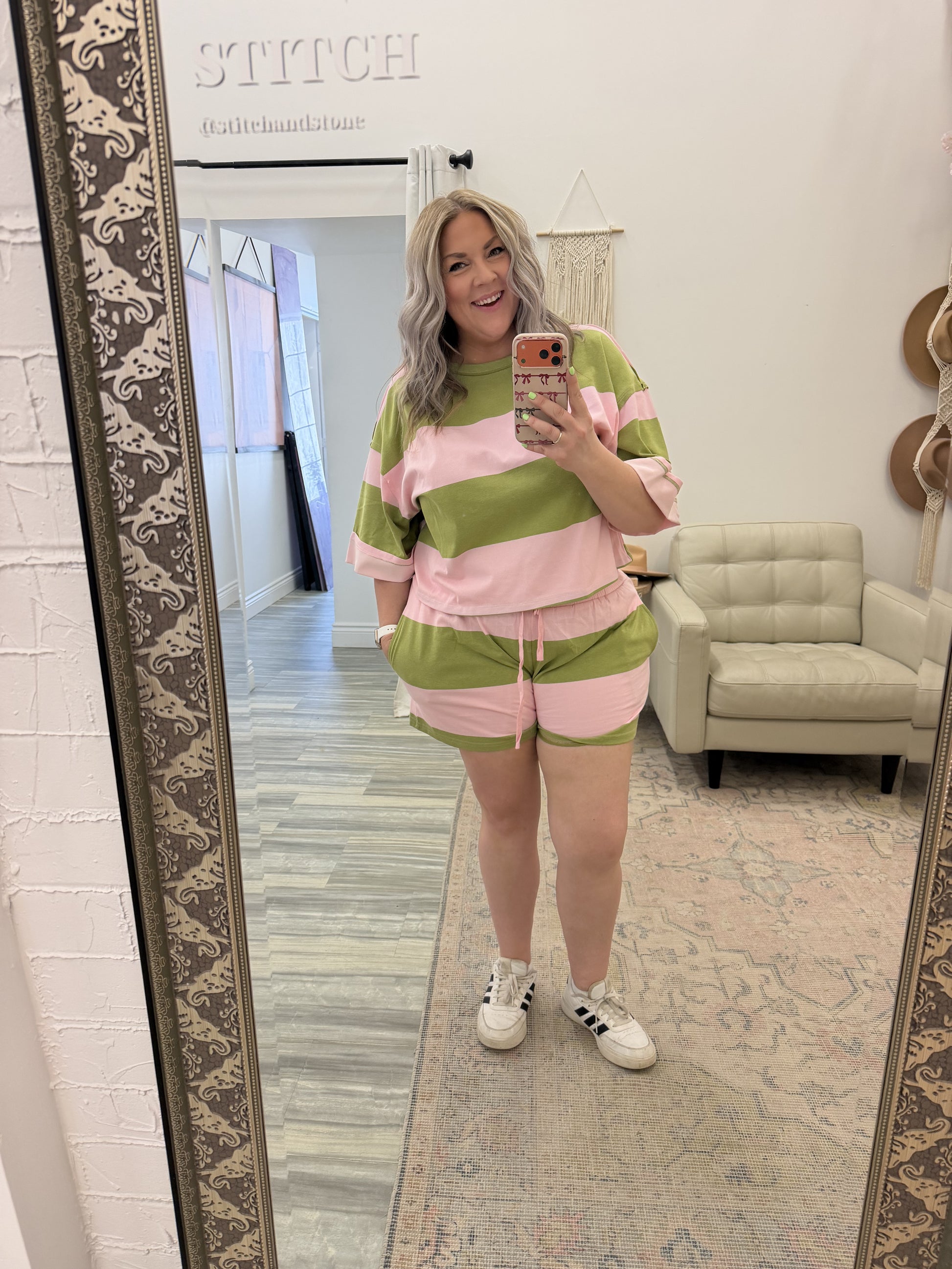 Person taking a mirror selfie wearing a pink and green outfit in a room with a large mirror.