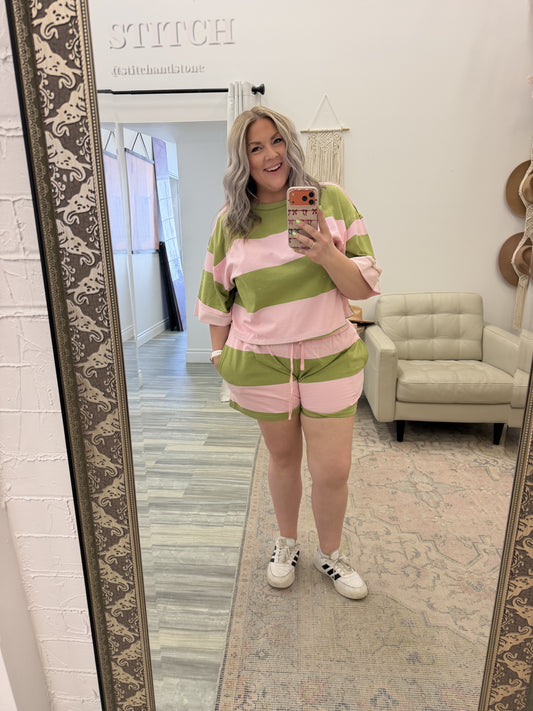Person taking a mirror selfie wearing a pink and green outfit in a room with a large mirror.