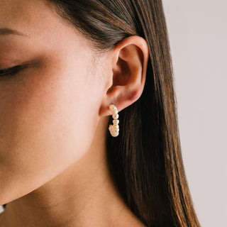 Close-up of a person wearing pearl hoop earrings with a neutral background