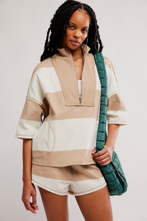 Woman wearing a beige and white outfit holding a green bag against a plain background