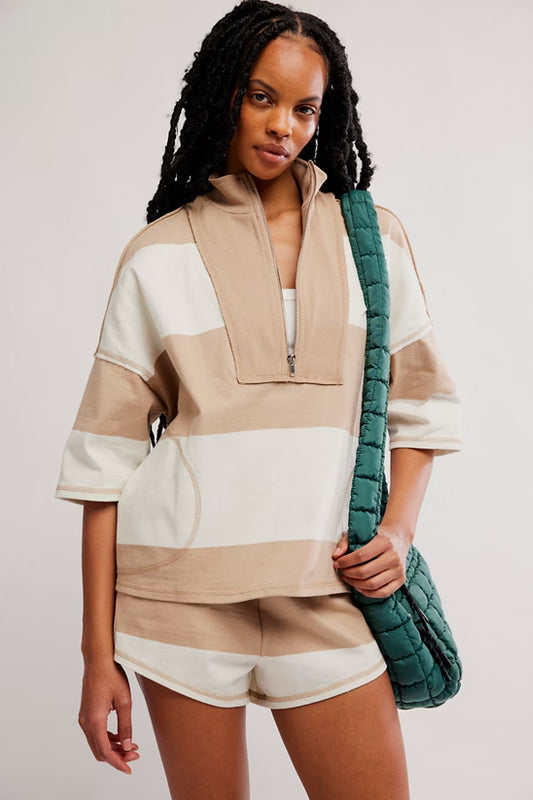 Woman wearing a beige and white outfit holding a green bag against a plain background