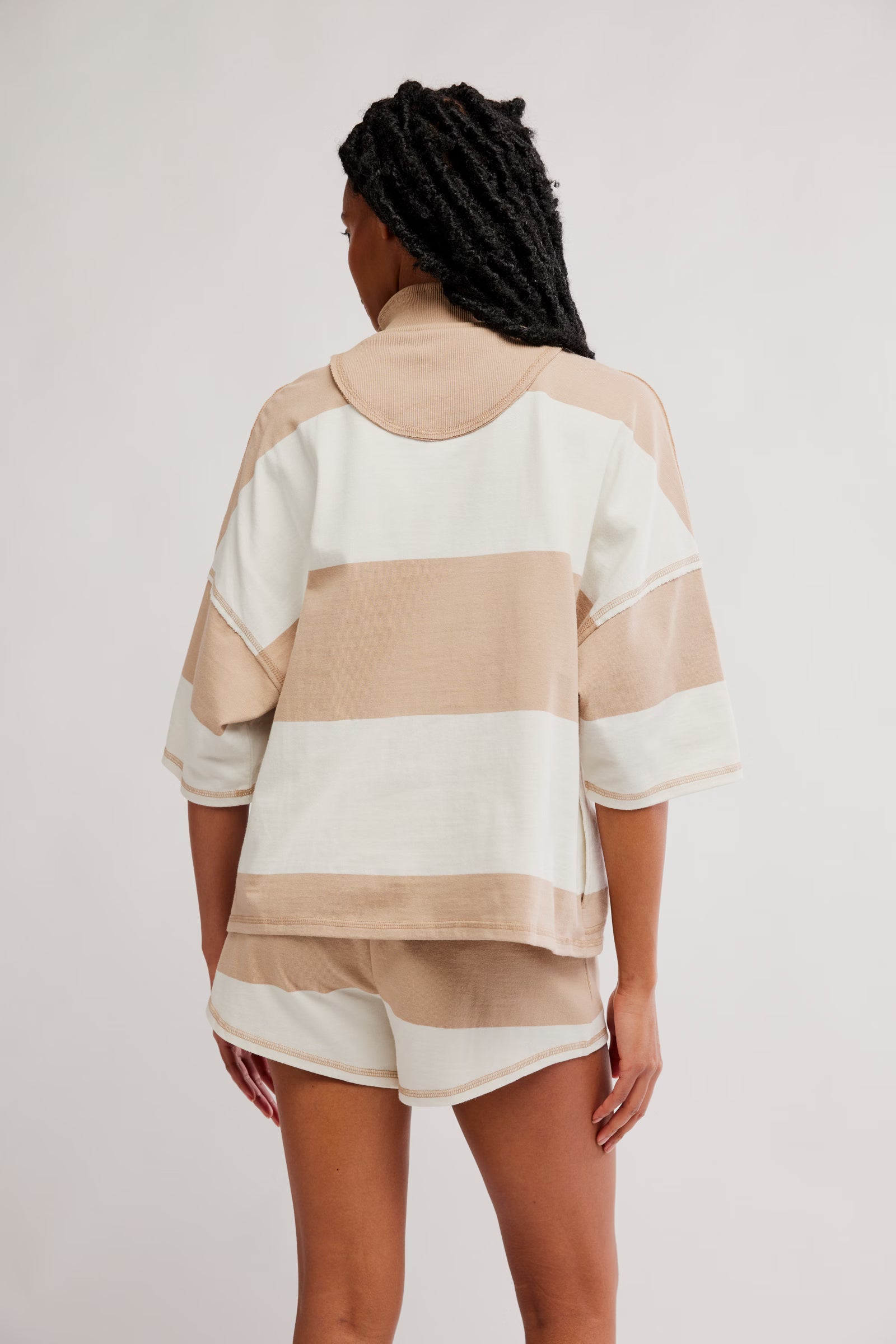 Person wearing a beige and white striped shirt with shorts on a plain background