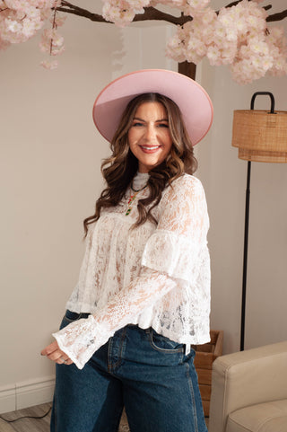 Woman wearing a white lace blouse and pink hat indoors with cherry blossom branches.