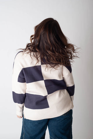 Person wearing a white sweater with blue checkered pattern on a plain background