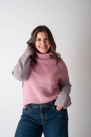 Woman wearing a pink turtleneck sweater with gray sleeves against a white background