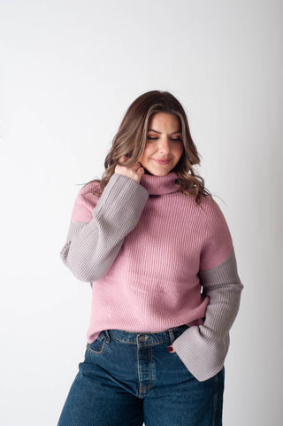 Woman wearing a pink sweater with gray sleeves against a white background