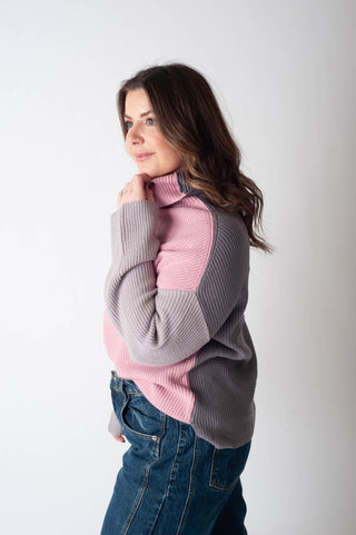 Woman wearing a gray and pink sweater with blue jeans on a white background