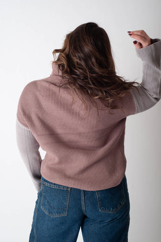 Person wearing a two-tone sweater and blue jeans against a white background