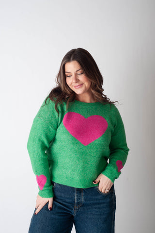 Woman wearing a green sweater with a pink heart design on a plain background