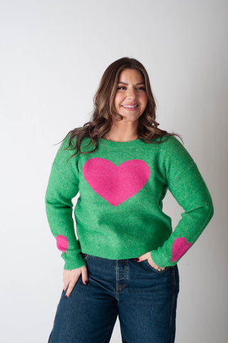 Woman wearing a green sweater with pink hearts on a plain background