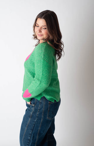 Woman wearing a green sweater with pink accents and blue jeans on a white background