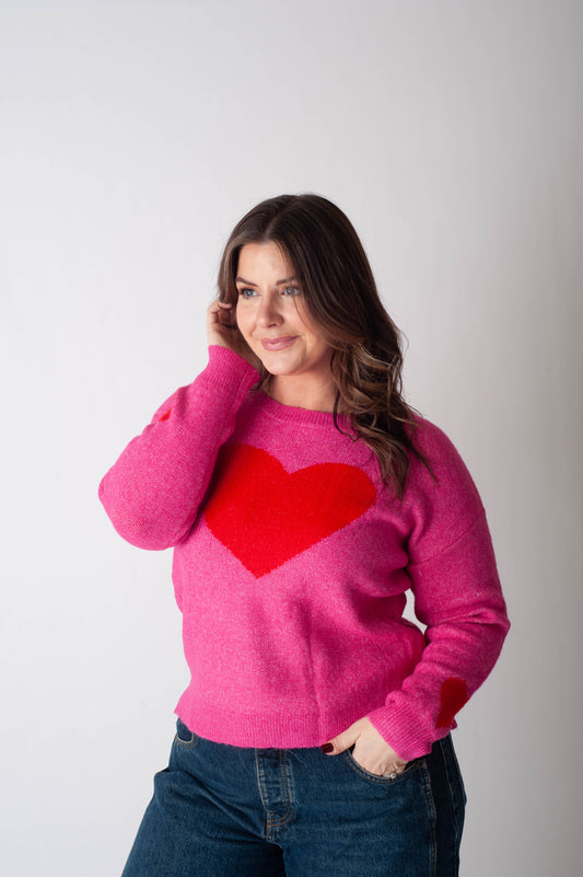 Woman wearing a pink sweater with a red heart design on a plain background