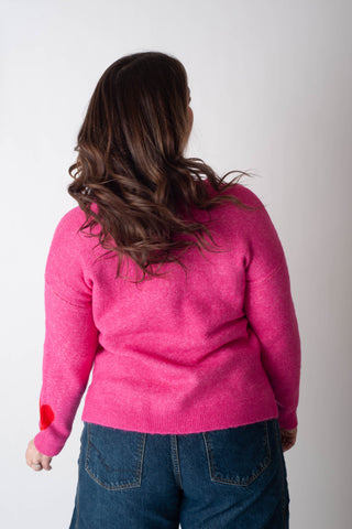 Person wearing a pink sweater with red accents on a plain background