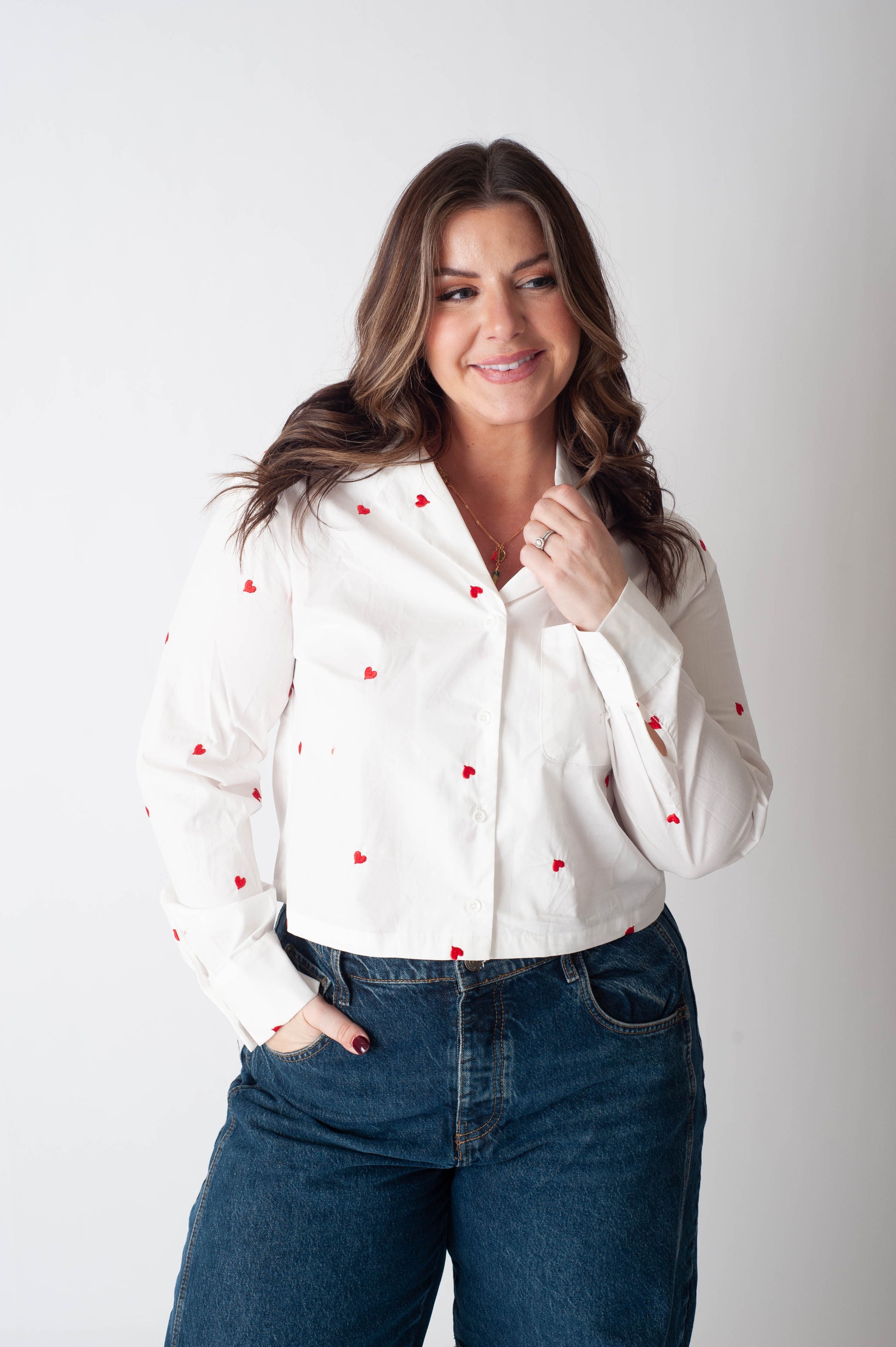 Woman wearing a white blouse with red polka dots and blue jeans on a plain background