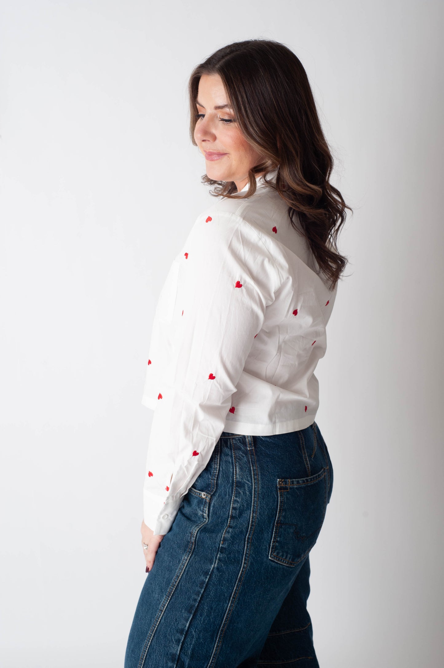 Woman wearing a white blouse with red patterns and blue jeans against a white background