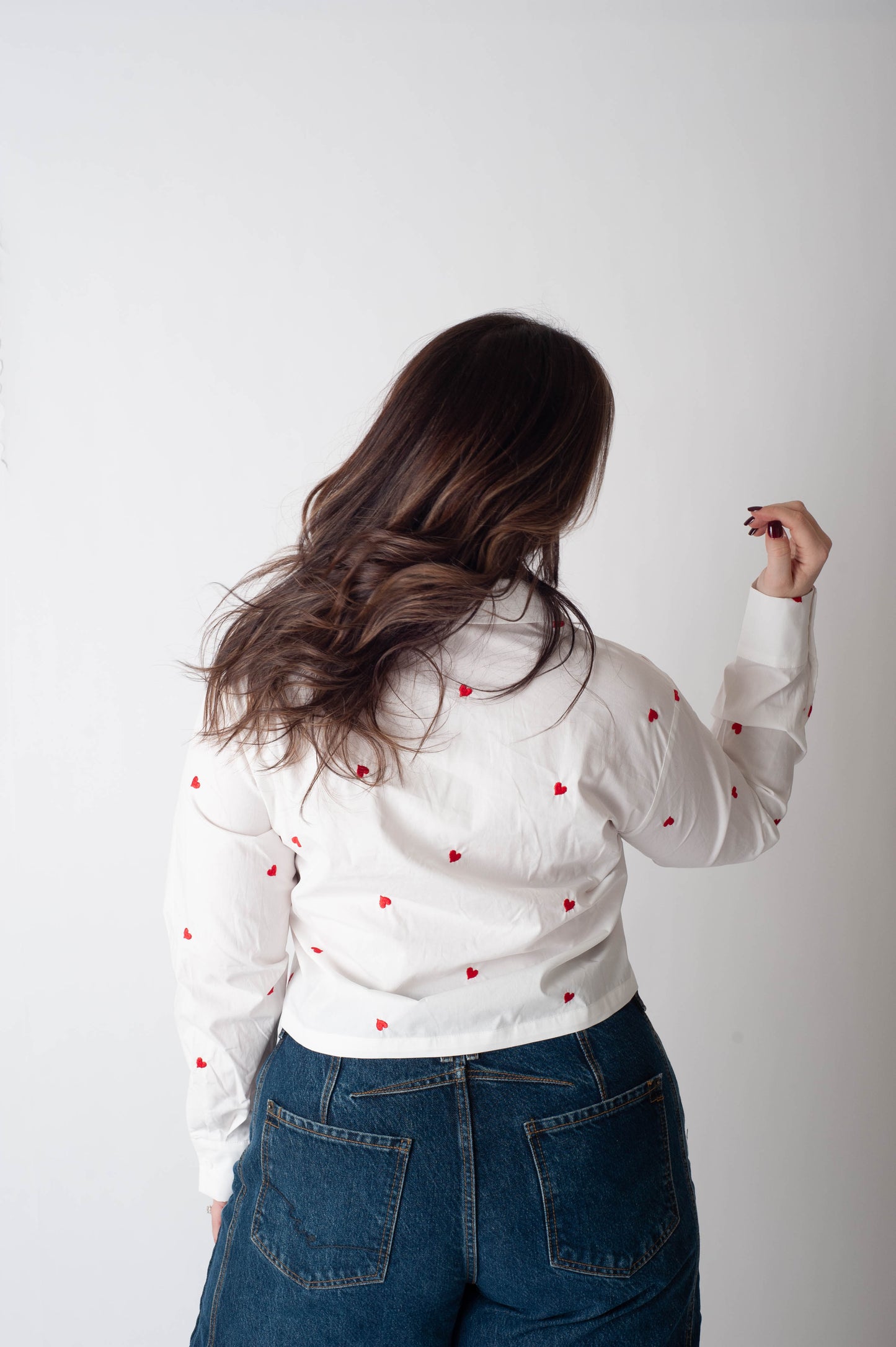 Person wearing a white blouse with red patterns and blue jeans on a plain background