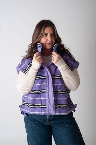 Woman wearing a purple striped vest over a white sweater on a plain background