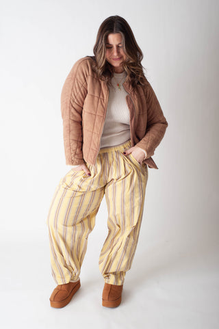 Woman wearing a brown jacket, white shirt, and yellow striped pants on a white background