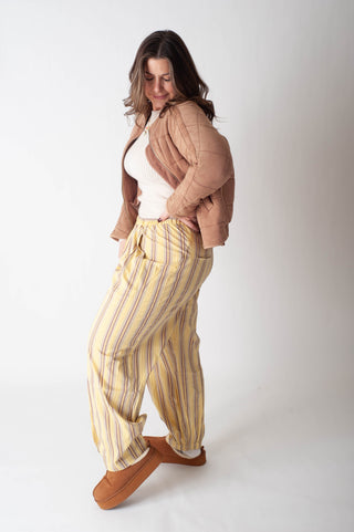 Woman wearing a beige jacket, white top, and yellow striped pants on a white background