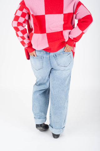 Person wearing a red and pink checkered sweater with light blue jeans on a white background