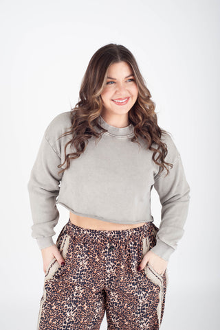 Woman wearing a gray cropped sweatshirt and leopard print pants on a white background