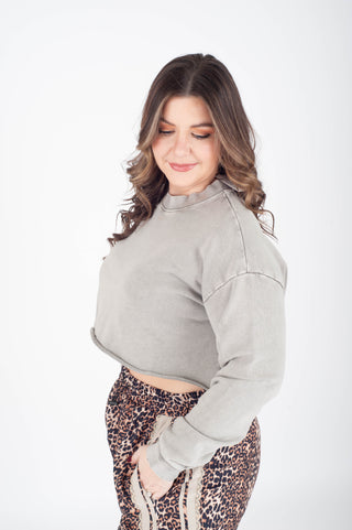 Woman wearing a gray cropped sweatshirt and leopard print pants on a white background