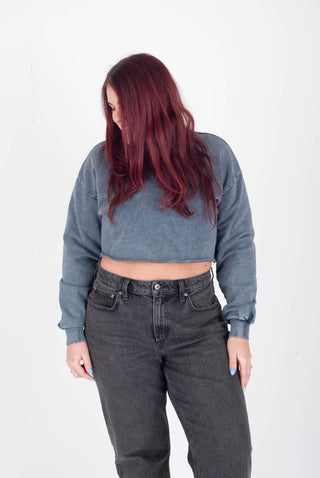 Person wearing a gray cropped sweatshirt and dark jeans on a white background