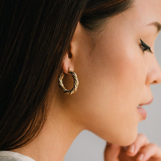 Close-up of a woman wearing a gold hoop earring against a neutral background