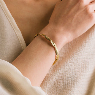 Gold bracelet on a wrist with a neutral background