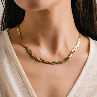 Gold necklace worn by a person against a neutral background