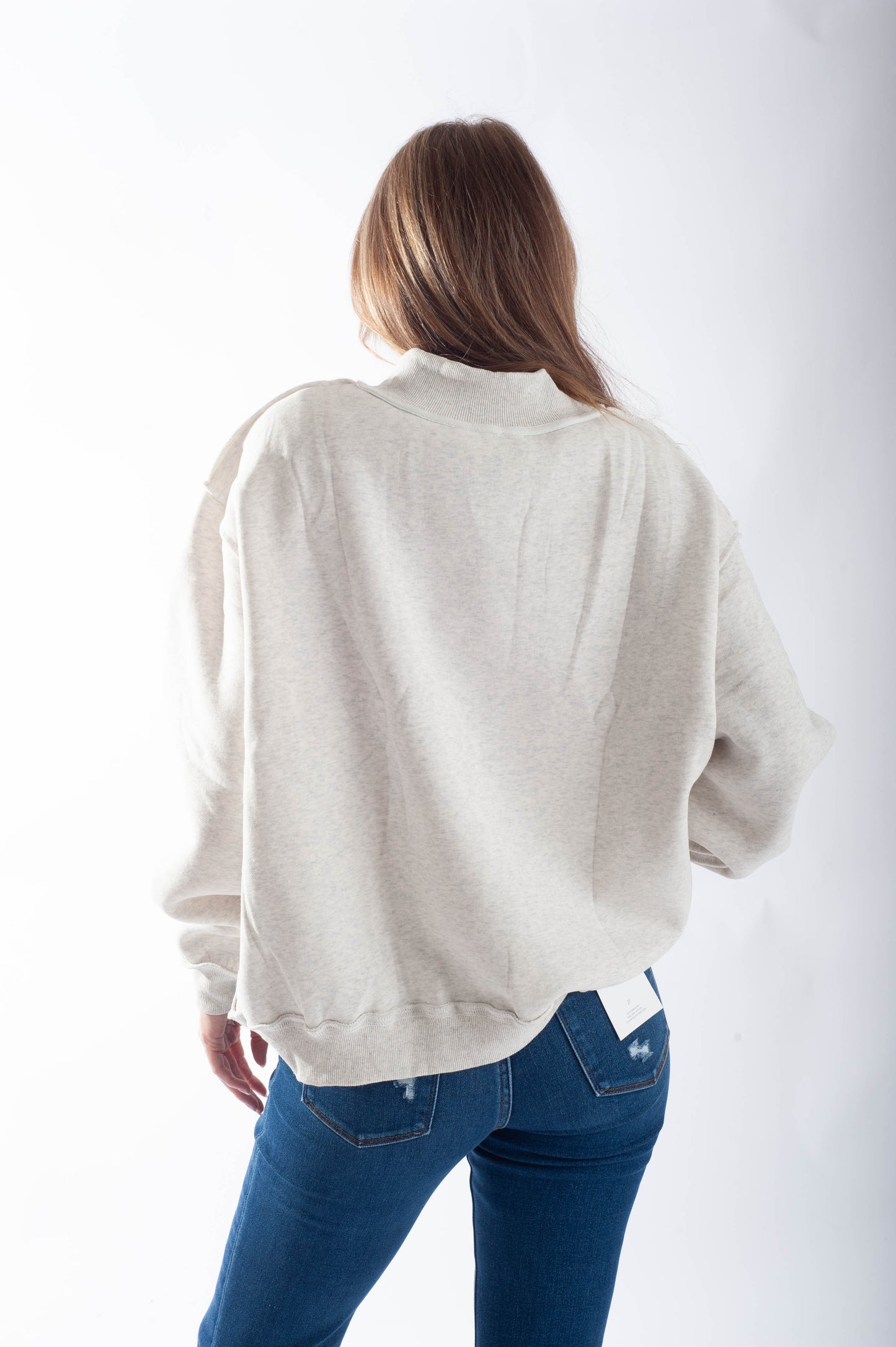 Person wearing a light gray jacket and blue jeans on a white background