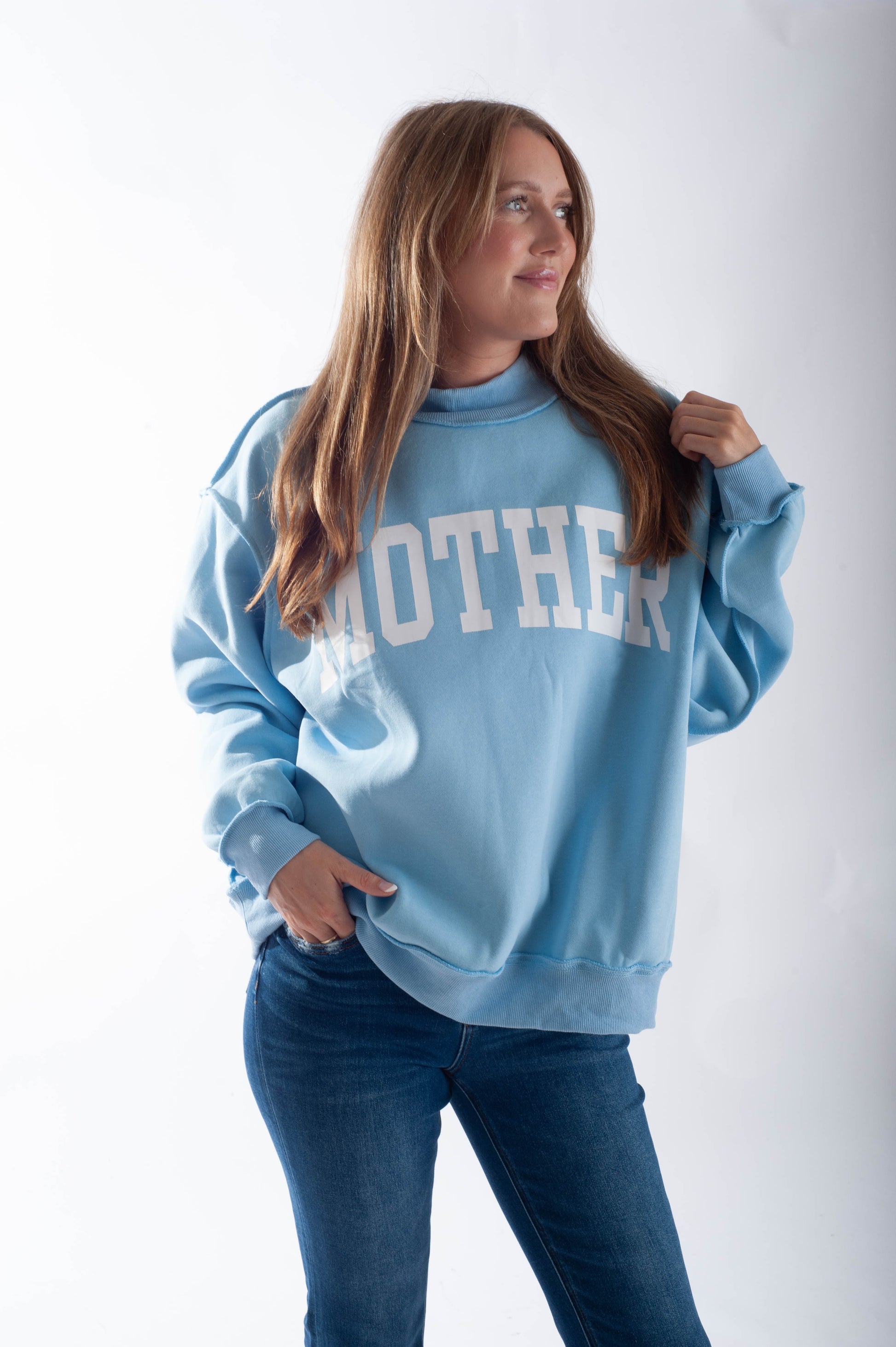 Woman wearing a light blue sweatshirt with 'MOTHER' printed on it against a white background