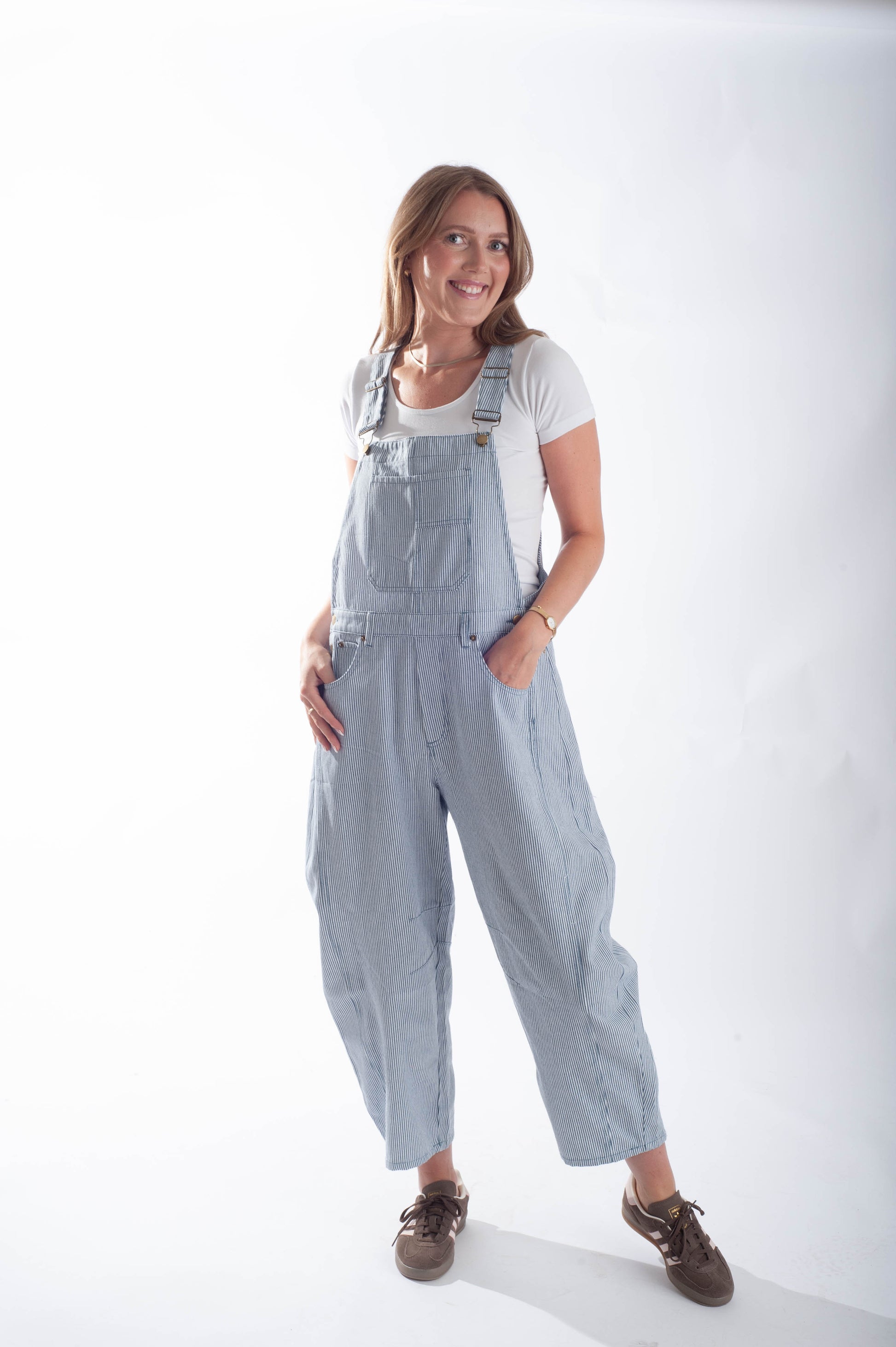Woman wearing light blue denim overalls on a white background