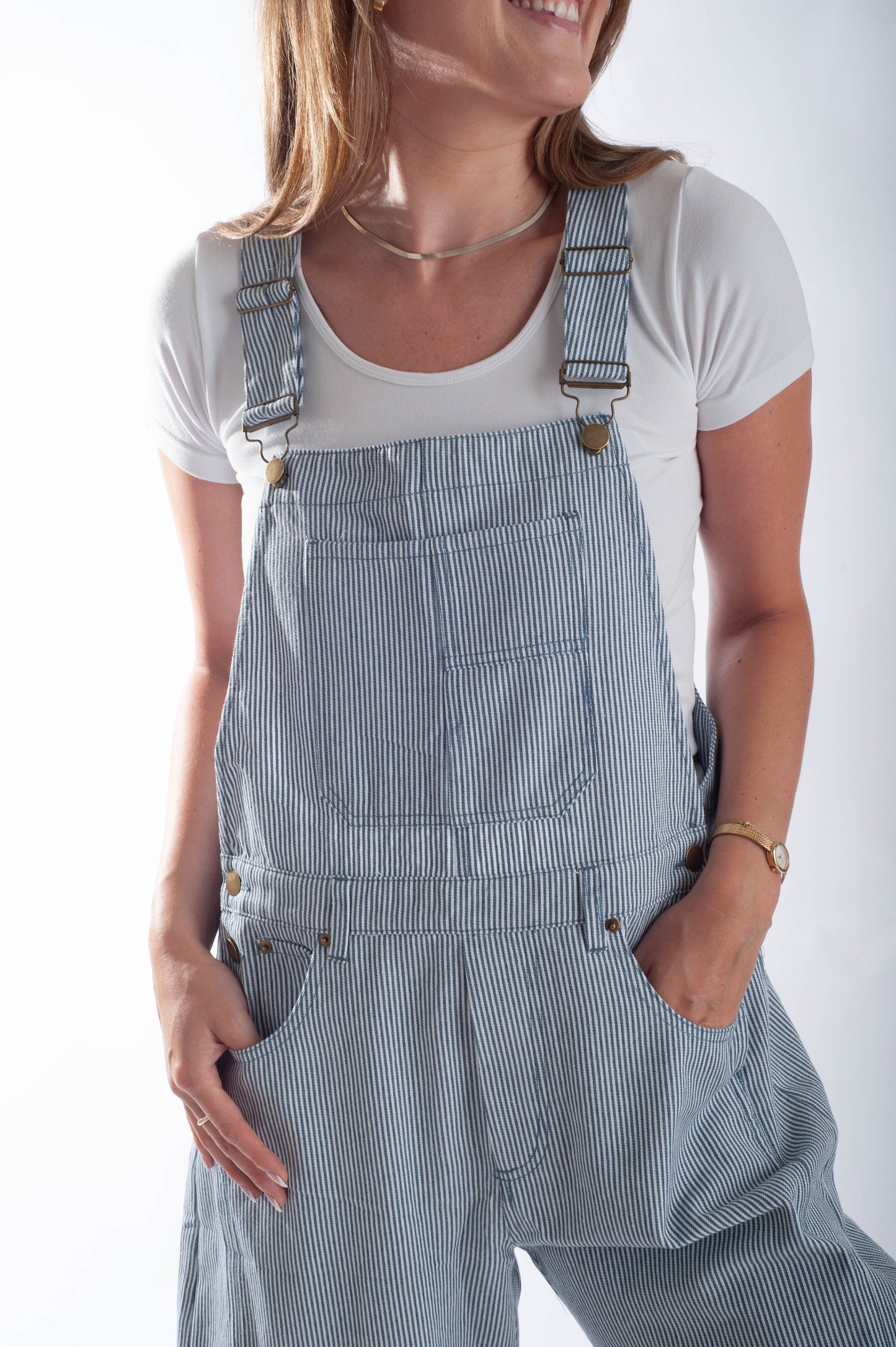 Person wearing blue striped overalls with a white shirt underneath on a plain background