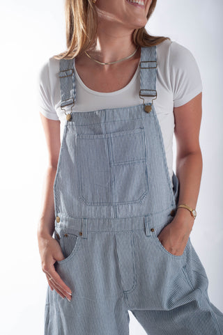 Person wearing blue striped overalls with a white shirt underneath on a plain background