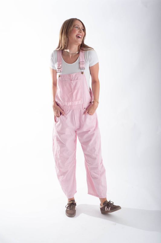 Woman wearing pink overalls and a white shirt on a white background