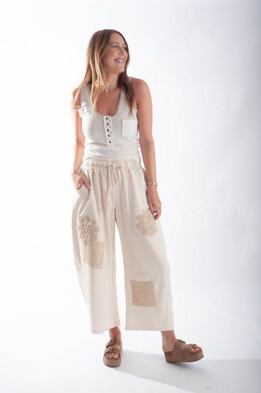 Woman wearing a white sleeveless top and beige wide-leg pants on a white background